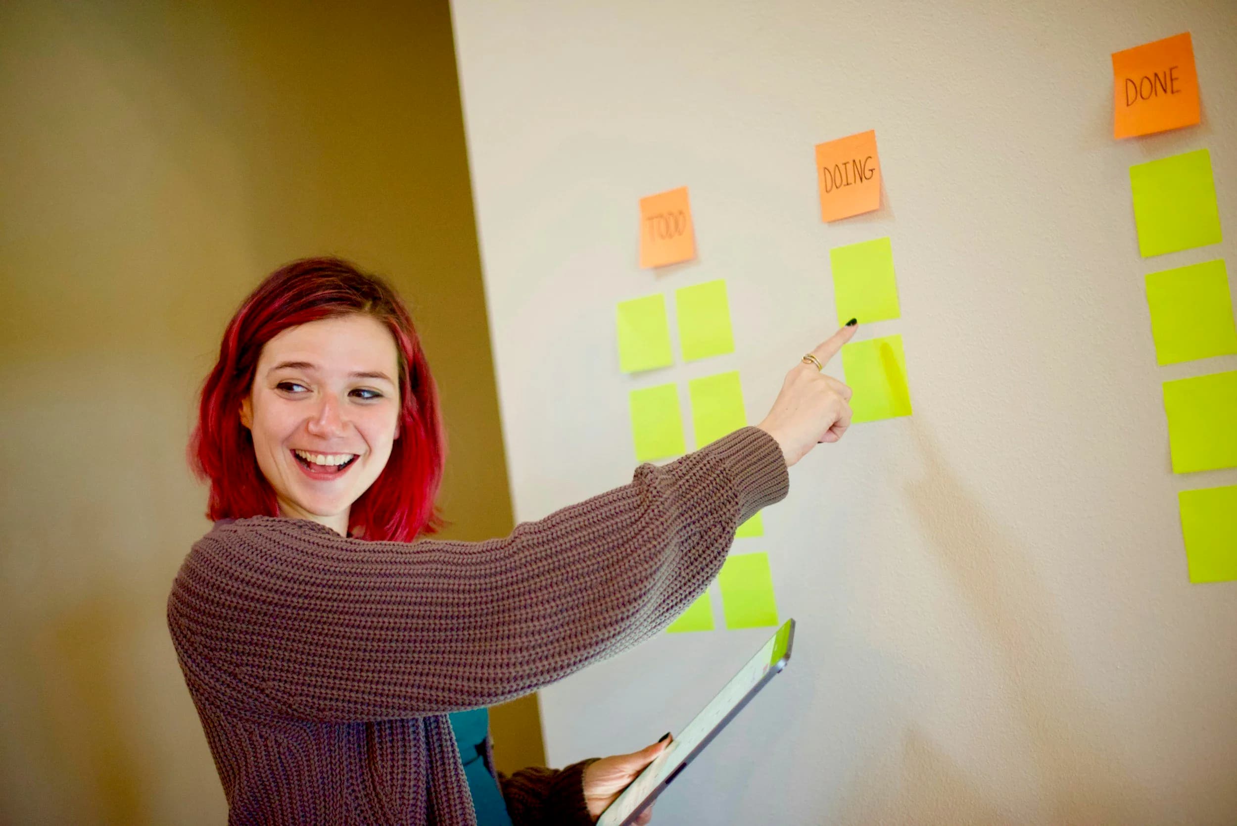 A facilitator smiling and pointing at sticky notes on a wall during a Certified ScrumMaster training session.